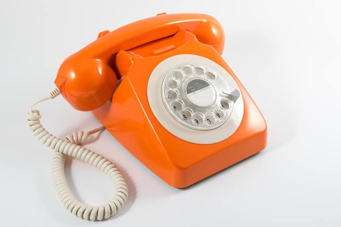 Bright orange vintage rotary dial telephone with a coiled cord, isolated on a white background