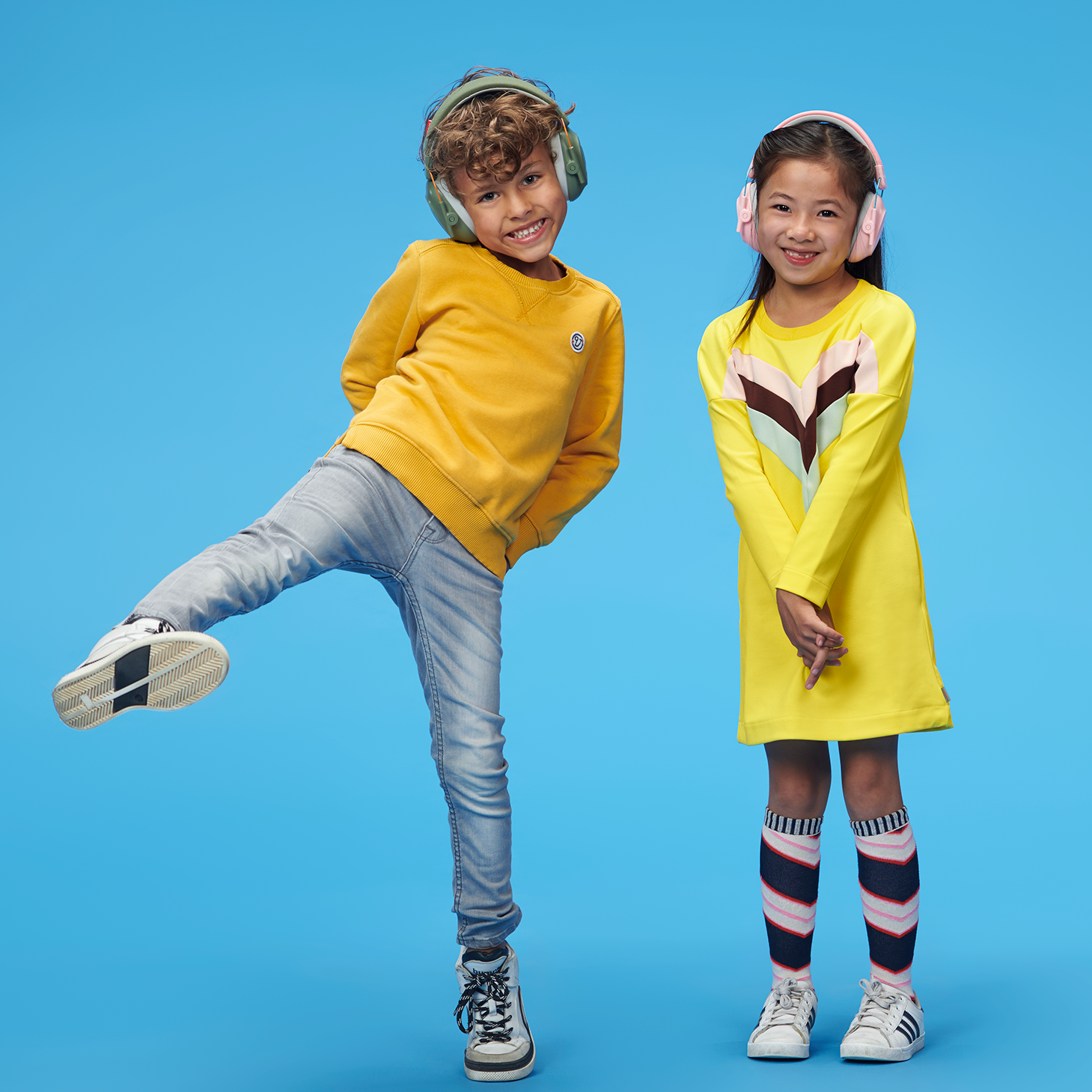 A boy and girl standing in front of a blue background wearing ear muffs smiling.