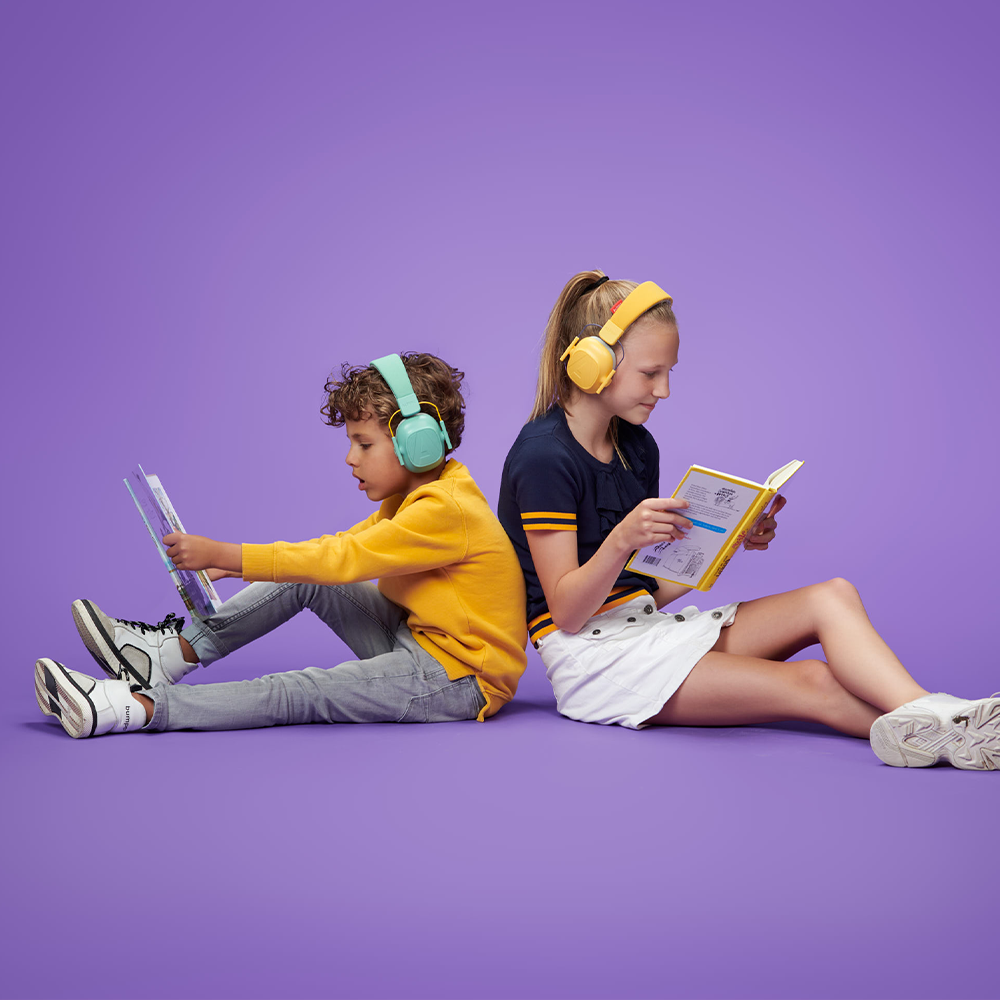 Two kids sitting back to back reading book wearing Yellow and a blue alpine ear muffs while readung