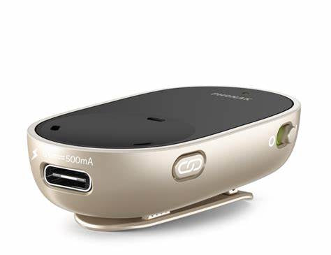 A compact, beige and black assistive listening Phonak PartnerMic device featuring a clip on the bottom for attaching to clothing. The front side has a USB port labeled '500mA' for charging, and a small button marked with a Bluetooth symbol. The device also has an on/off switch on the side and a sleek, curved design.